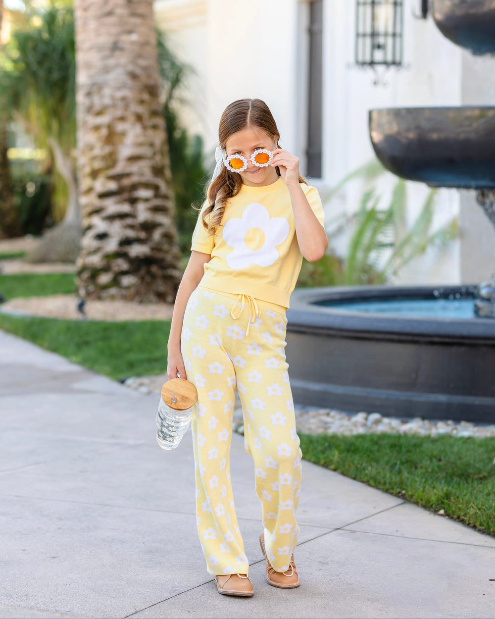young girl in daisy sunglasses wearing pastel yellow short sleeve knit sweater top with white retro flower design and matching sweater pants with white floral design