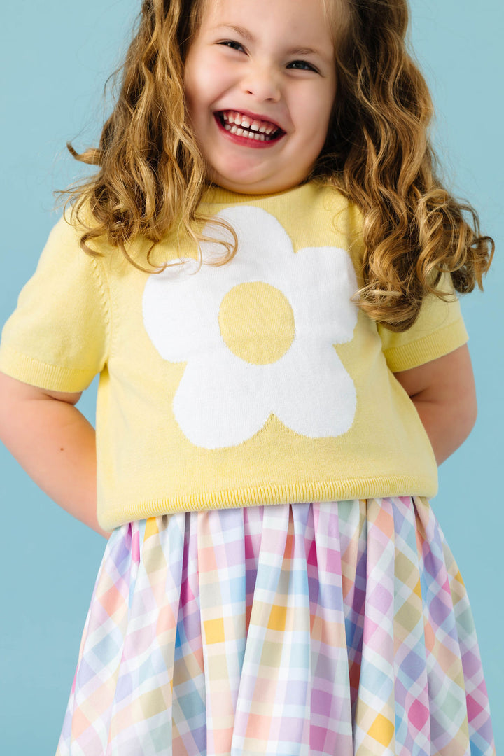young girl in pastel yellow flower sweater paired with pastel gingham twirl dress