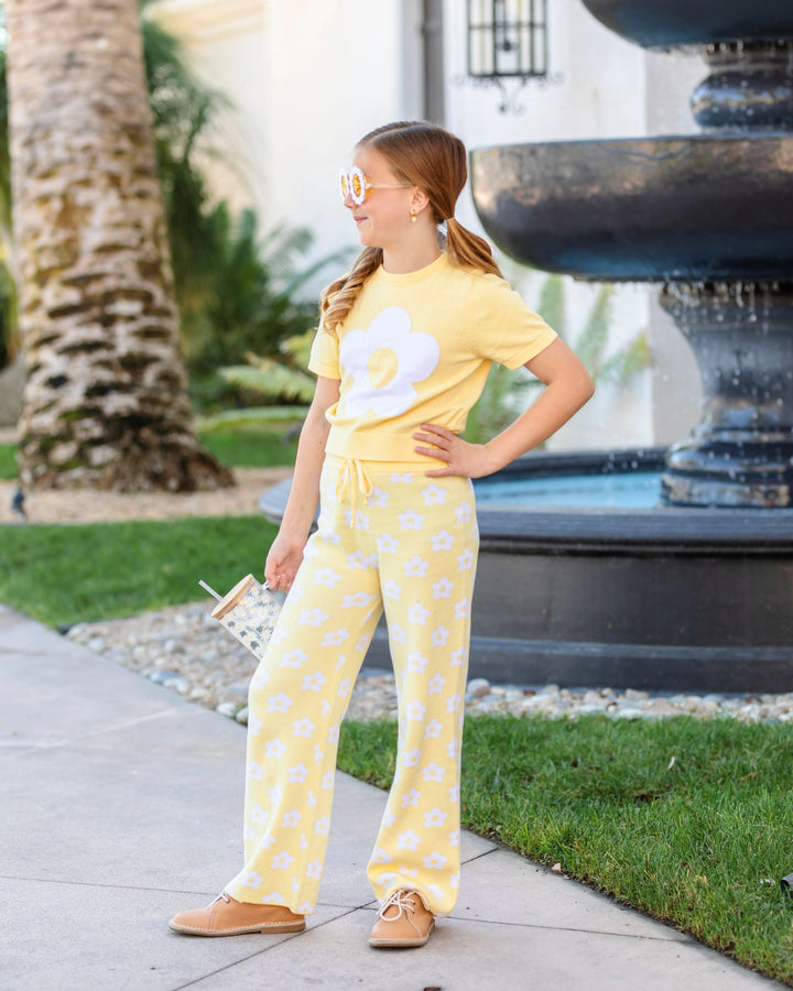 girl by fountain in pastel yellow short sleeve sweater with single white retro flower design and matching cotton knit sweater pants with all over white floral pattern