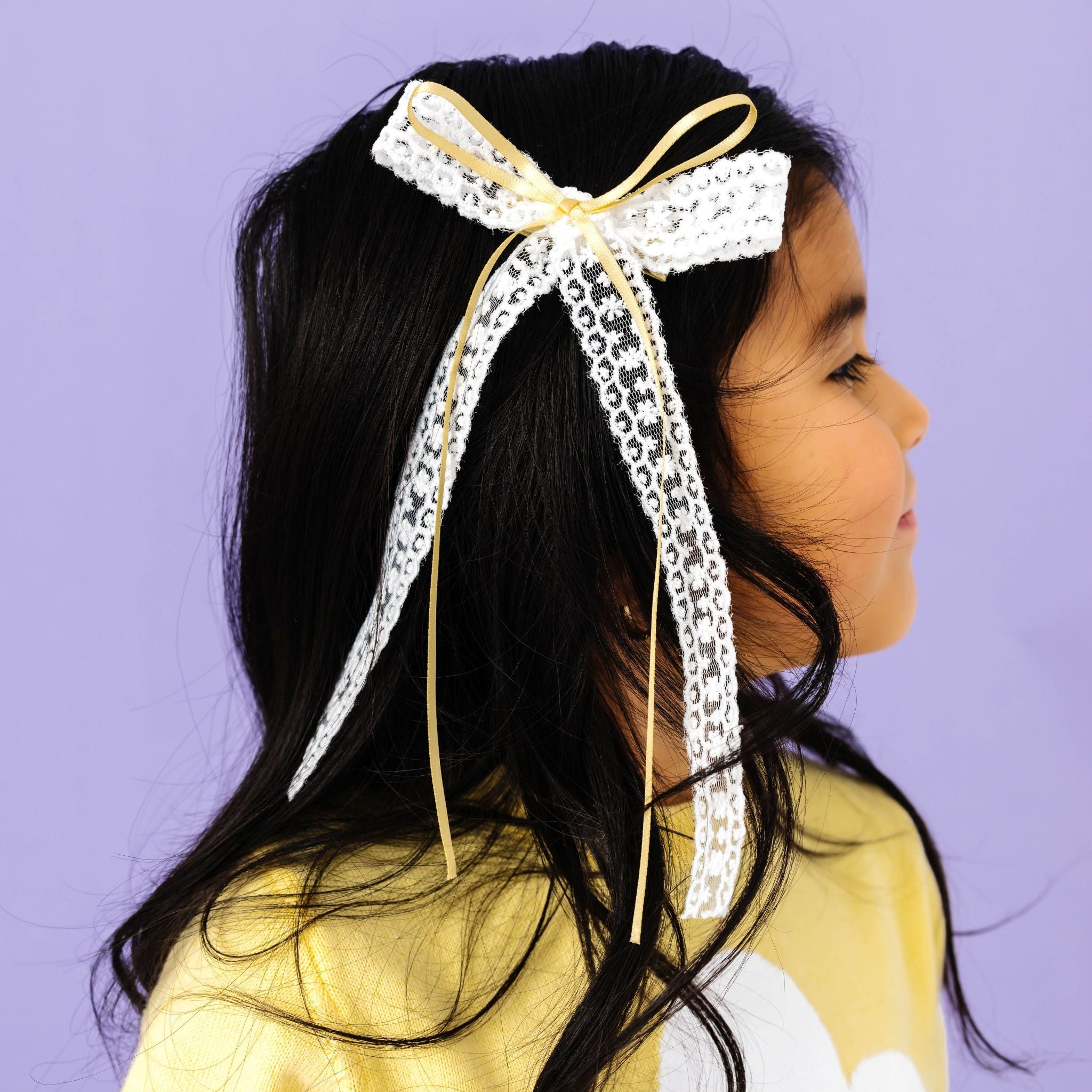 little girl in pastel yellow sweater set wearing matching white lace bow with pastel yellow satin ribbon accent on alligator clip