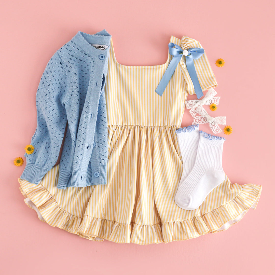 girls' light yellow and white pinstripe short sleeve twirl dress surrounded by yellow daisies paired with spring blue accessories and matching blue pointelle cotton knit cardigan