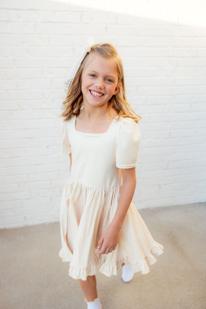 young girl in pastel yellow and white pinstripe spring twirl dress with matching bow and midi socks