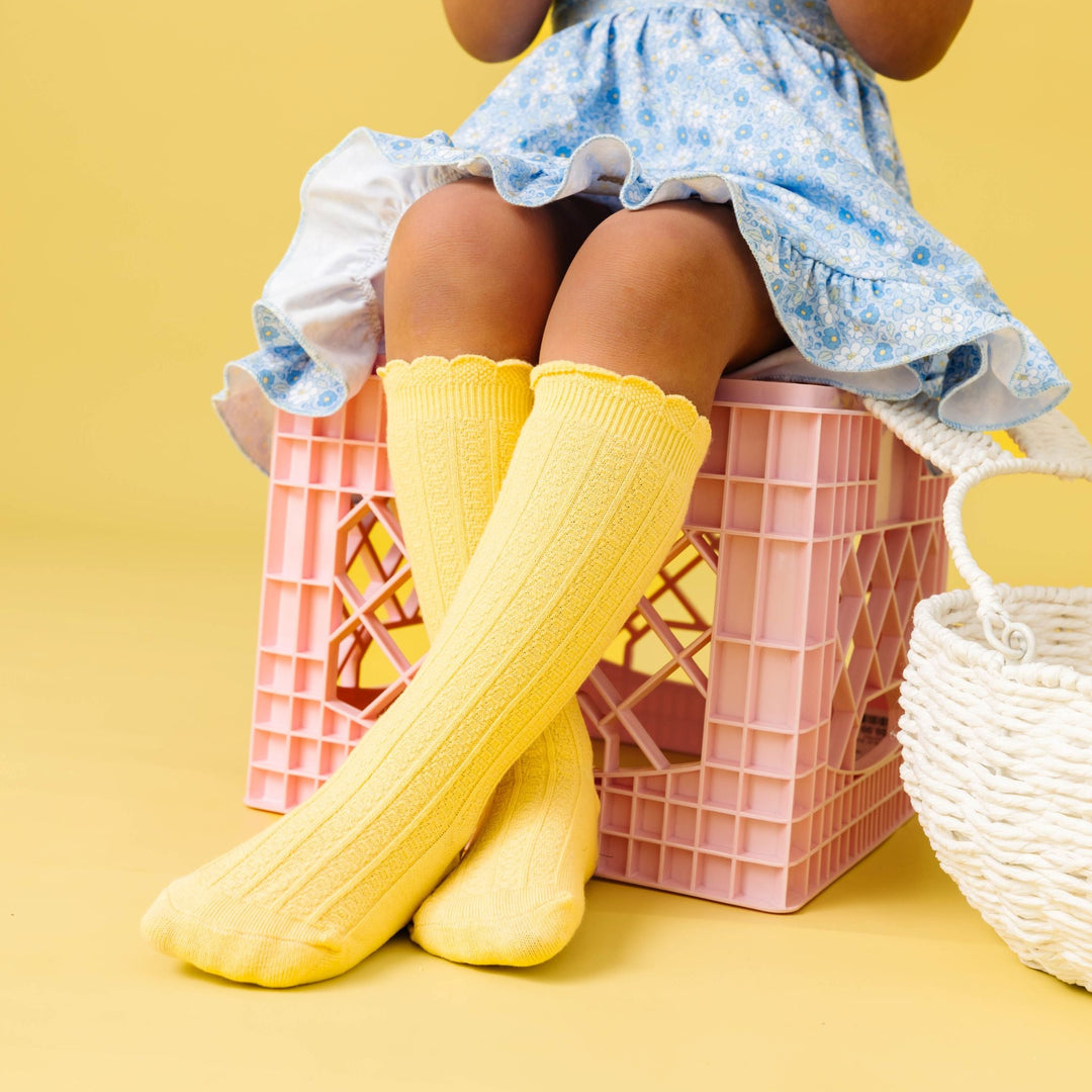 little girl sitting on crate in pastel blue floral spring twirl dress paired with light yellow knee socks with scalloped trim