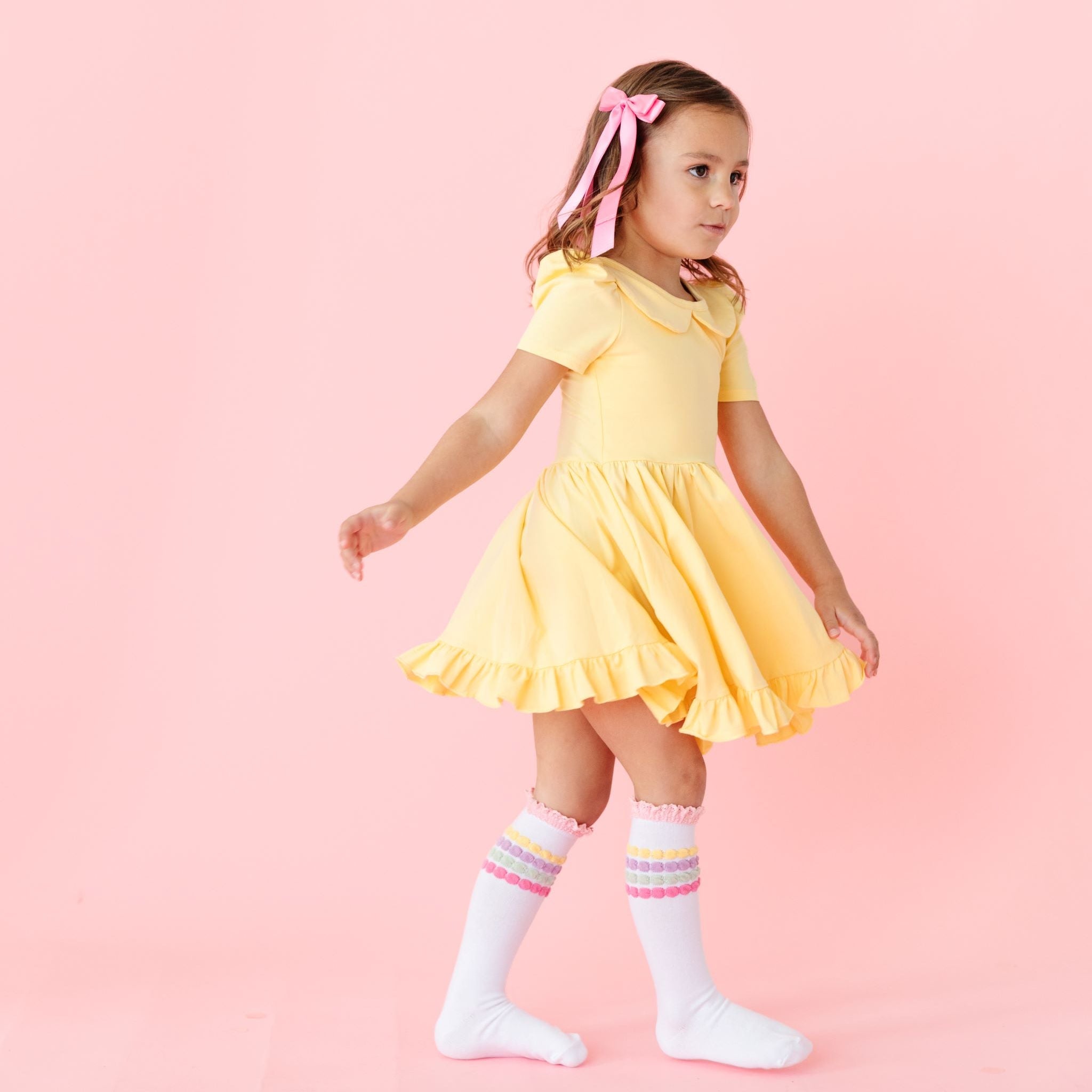 little girl in spring yellow twirl dress with matching pastel stripe knee highs and light pink satin bow