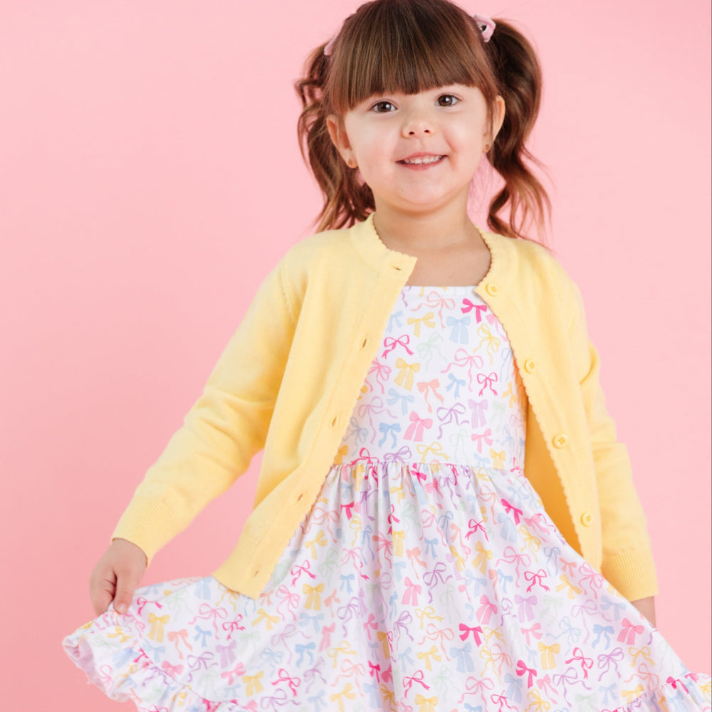 little girl in spring yellow cotton knit cardigan with scallop edge detail and matching white twirl dress with printed bows