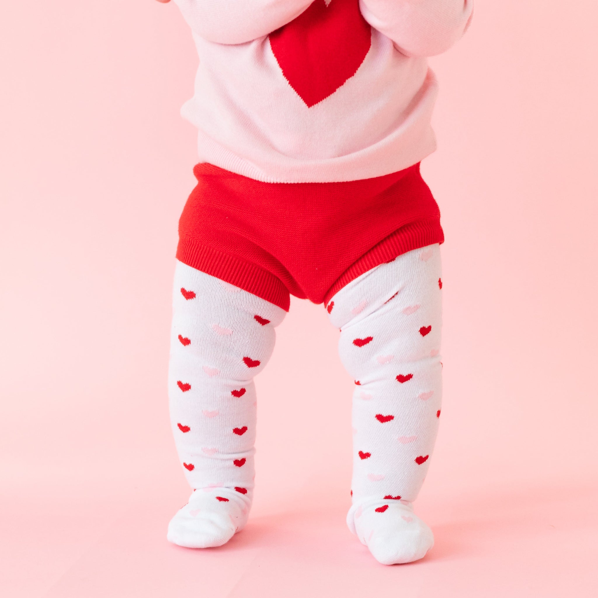 closeup of red cotton knit baby bloomers paired with patterned heart tights and matching pink heart sweater