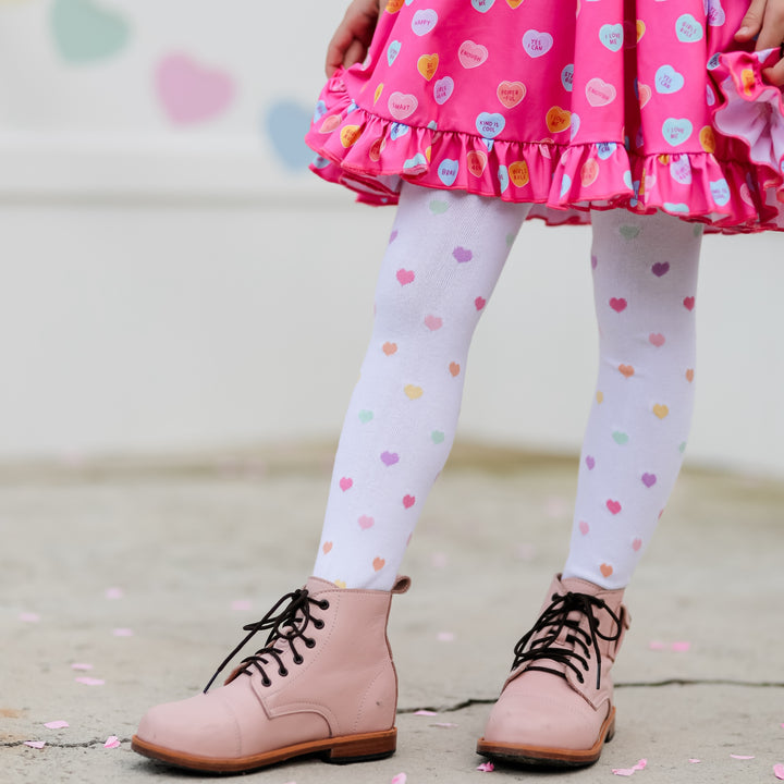 little girl wearing rainbow heart valentines day tights with light pink boots and candy heart dress