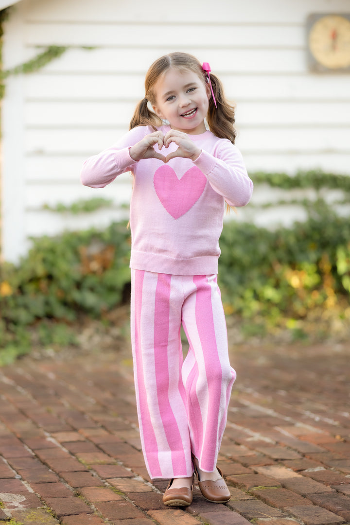 little girl with heart hands wearing two tone pink pullover sweater and striped two tone pink sweater pants for valentines day