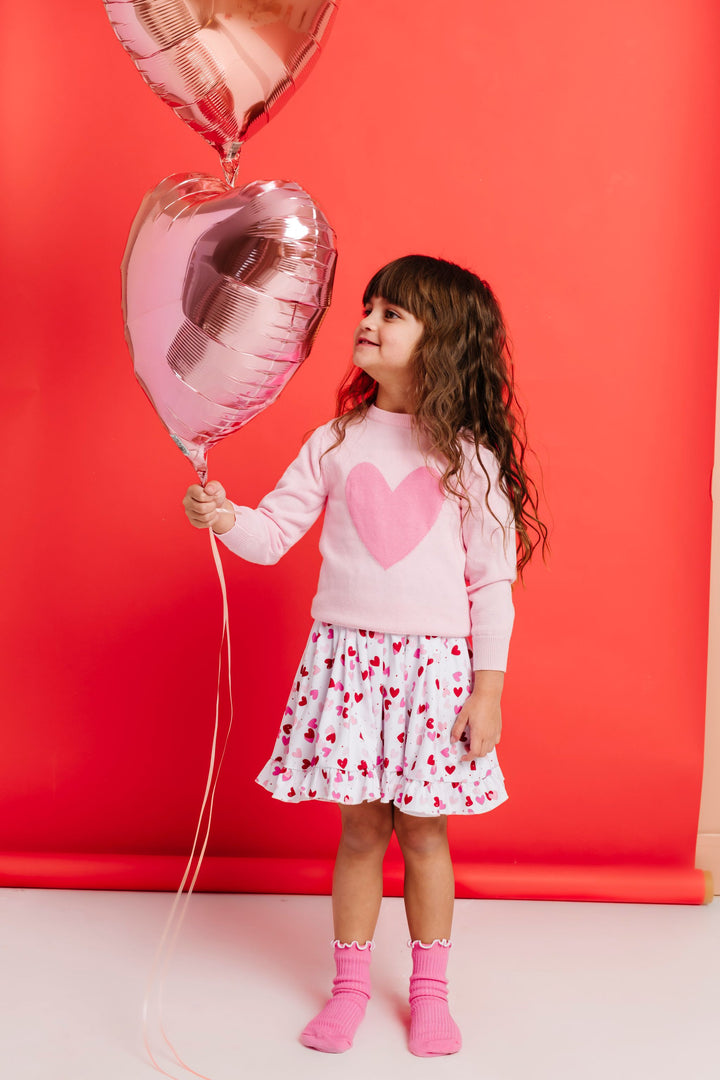 little girl holding heart balloons in white twirl dress with scattered heart print paired with two tine pink heart sweater and matching pink midi sock