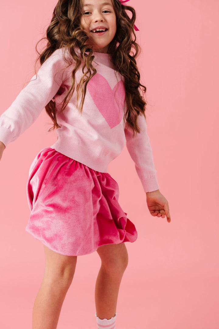 girl jumping in two tone pink heart pullover sweater and matching pink velvet skort
