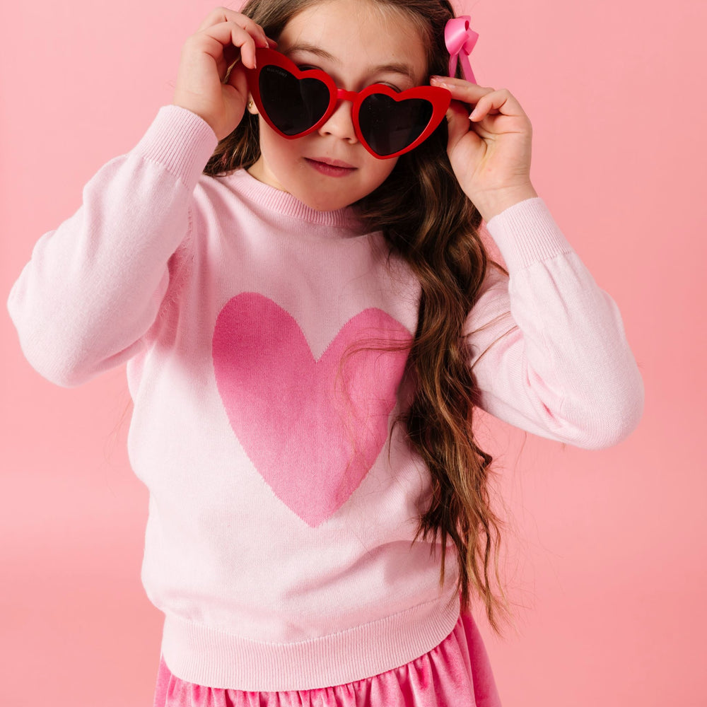 young girl wearing two tone pink knit sweater with heart design, pink satin bow, pink velvet skort and heart sunnies