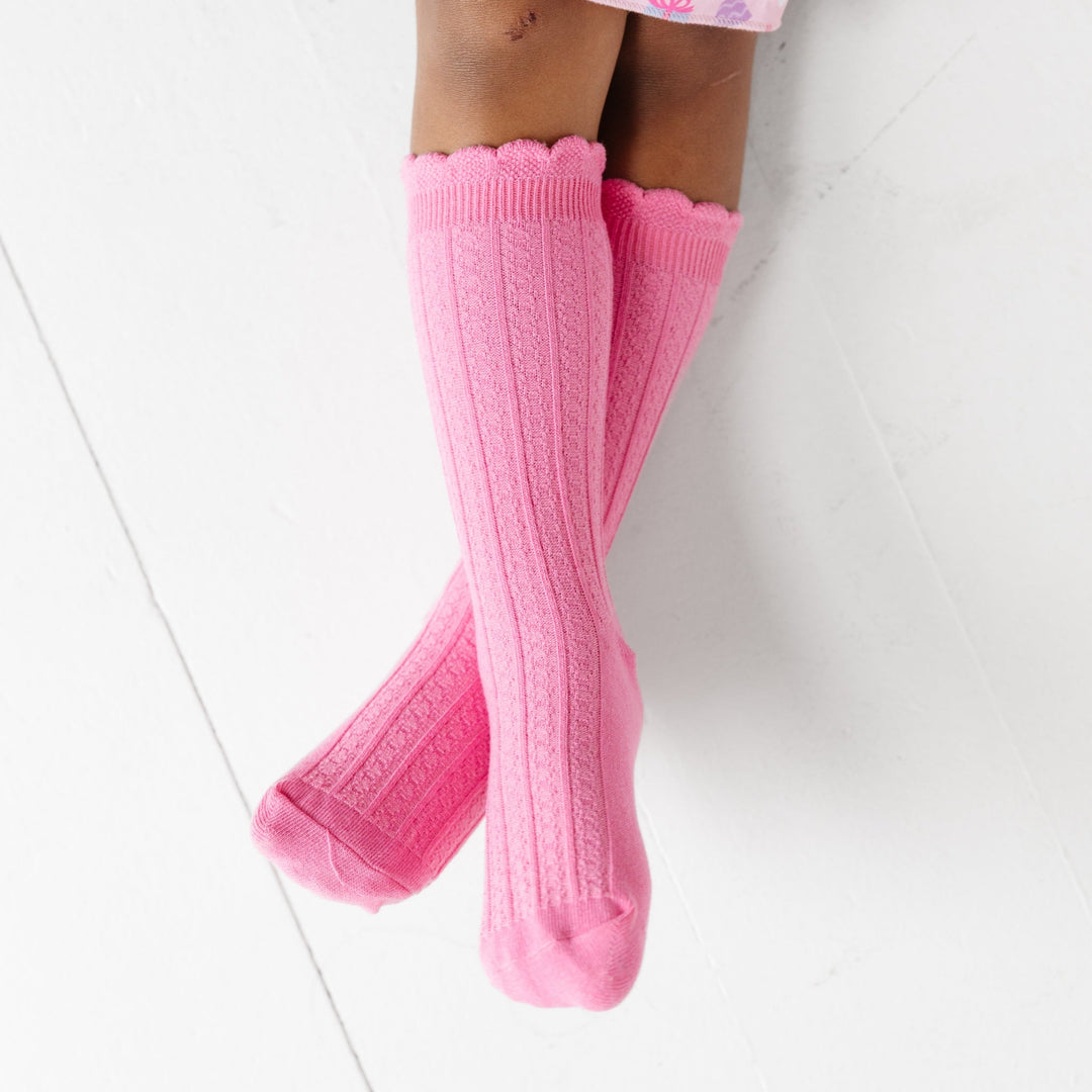 girl's legs crossed wearing  pink knee highs socks with dainty vertical knit pattern and scalloped trim