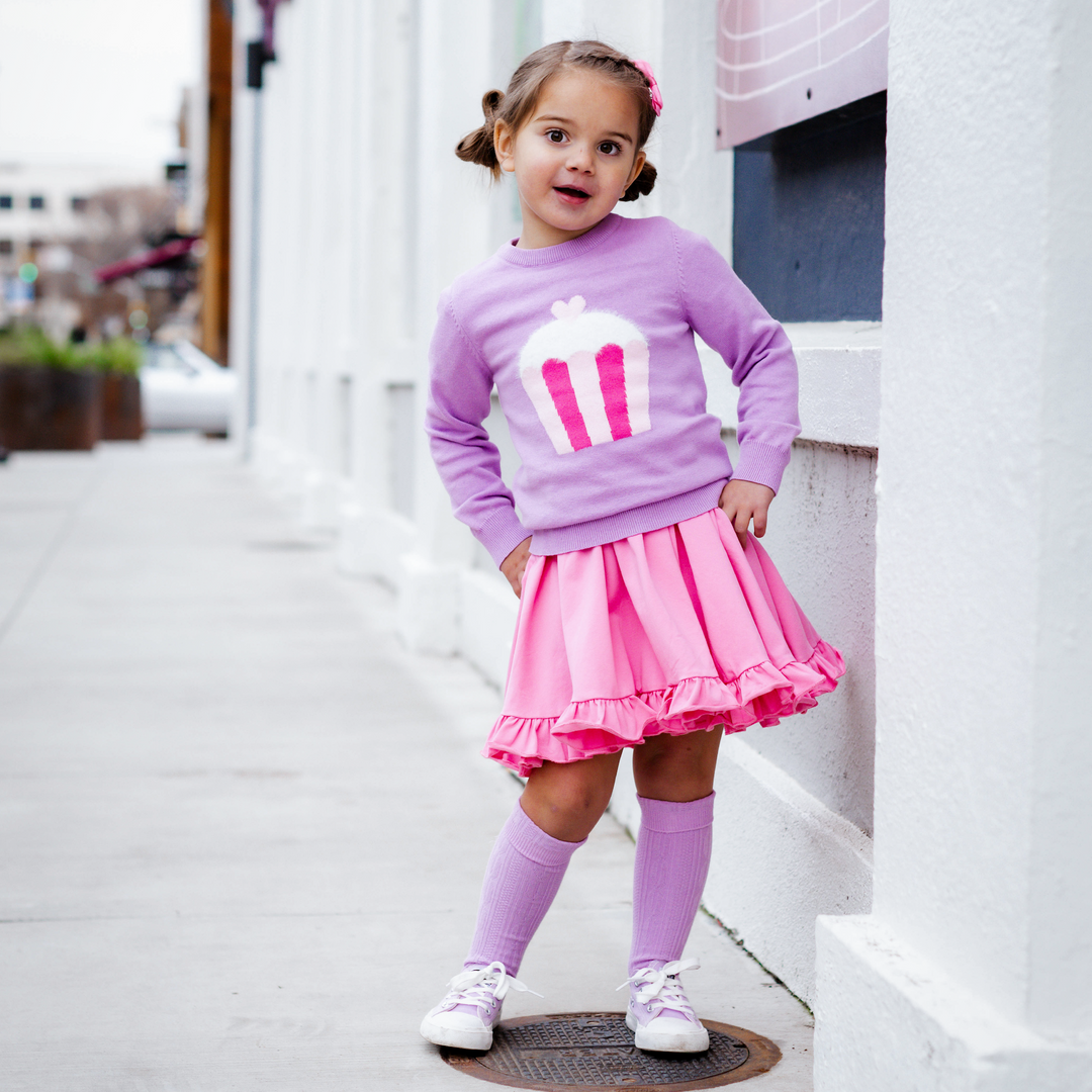 girl in pink twirl dress and purple sweater with fuzzy cupcake and matching knee high socks