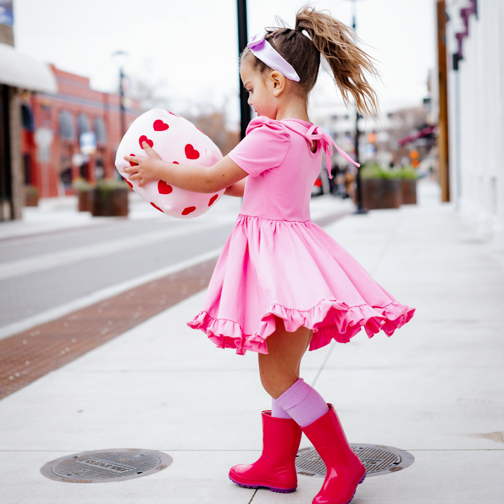 girl spinning in pink twirl dress with tie back and purple cable knit socks