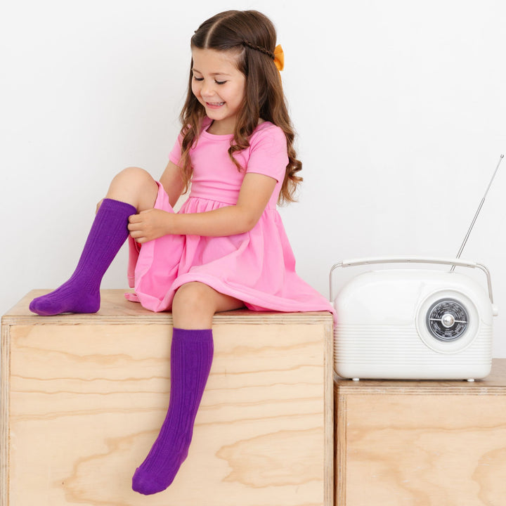 little girl pulling up purple knee sock wearing pink dress