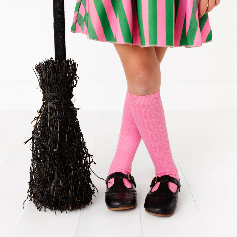 little girl with broom in pink cable knit knee high socks and wicked themed skort for Halloween