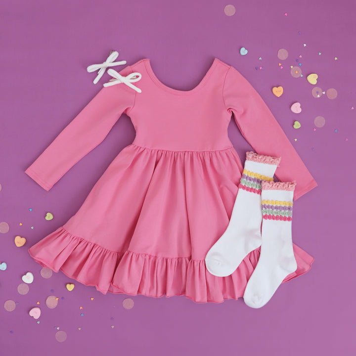 girls pink cotton twirl dress with long sleeves styled for valentine's Day with pastel striped knee highs and white yarn pigtail bows