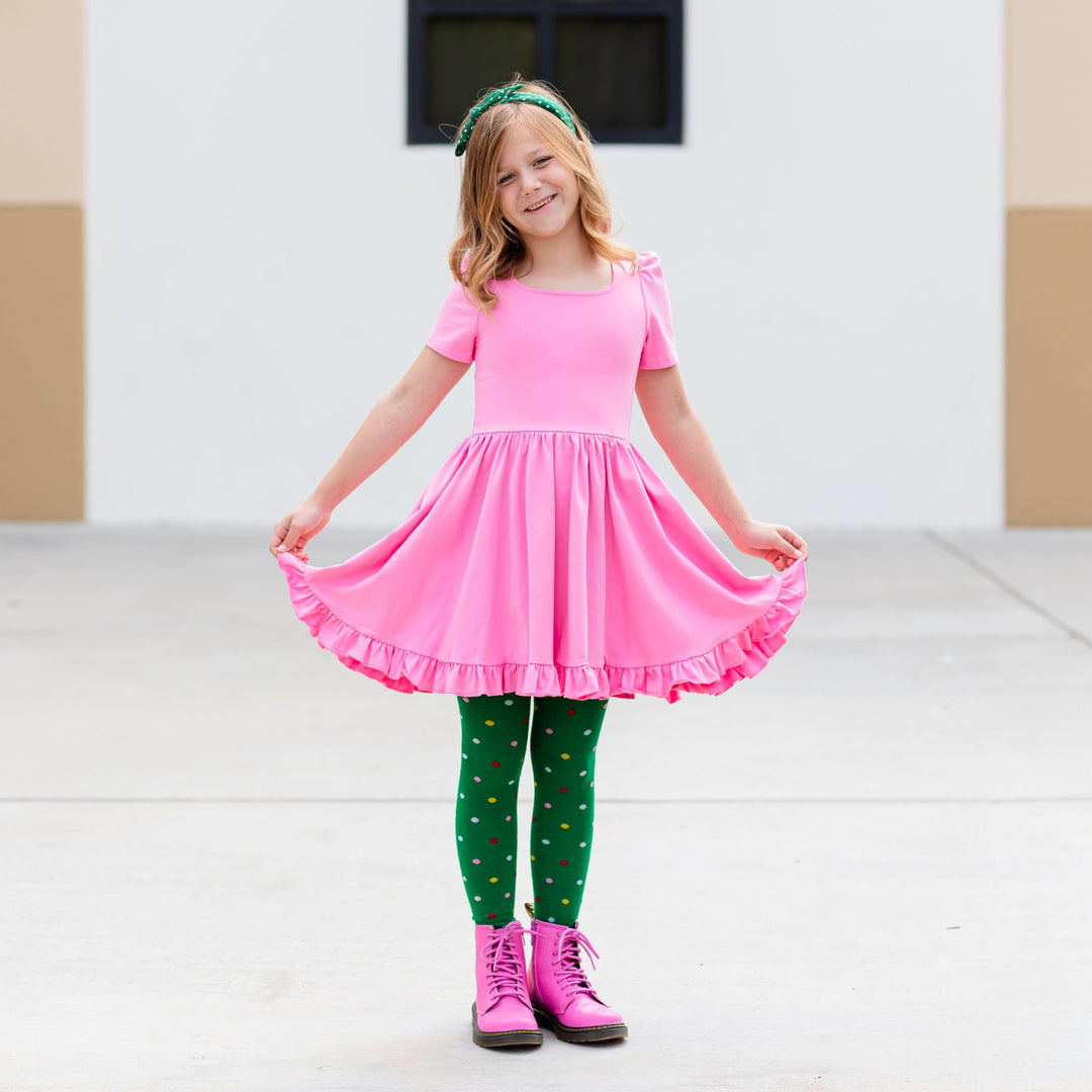 little girl in classic pink cotton party dress and matching green tights and headband with colorful dots