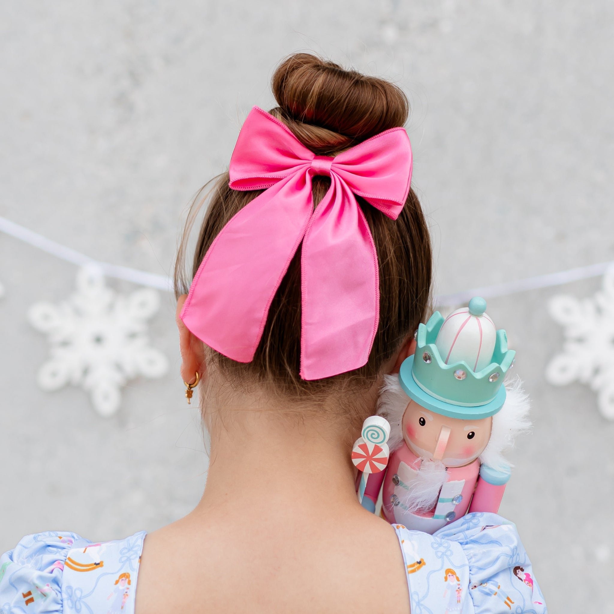 young girl holding nutcracker toy in matching dress with pink satin ribbon hair bow on clip