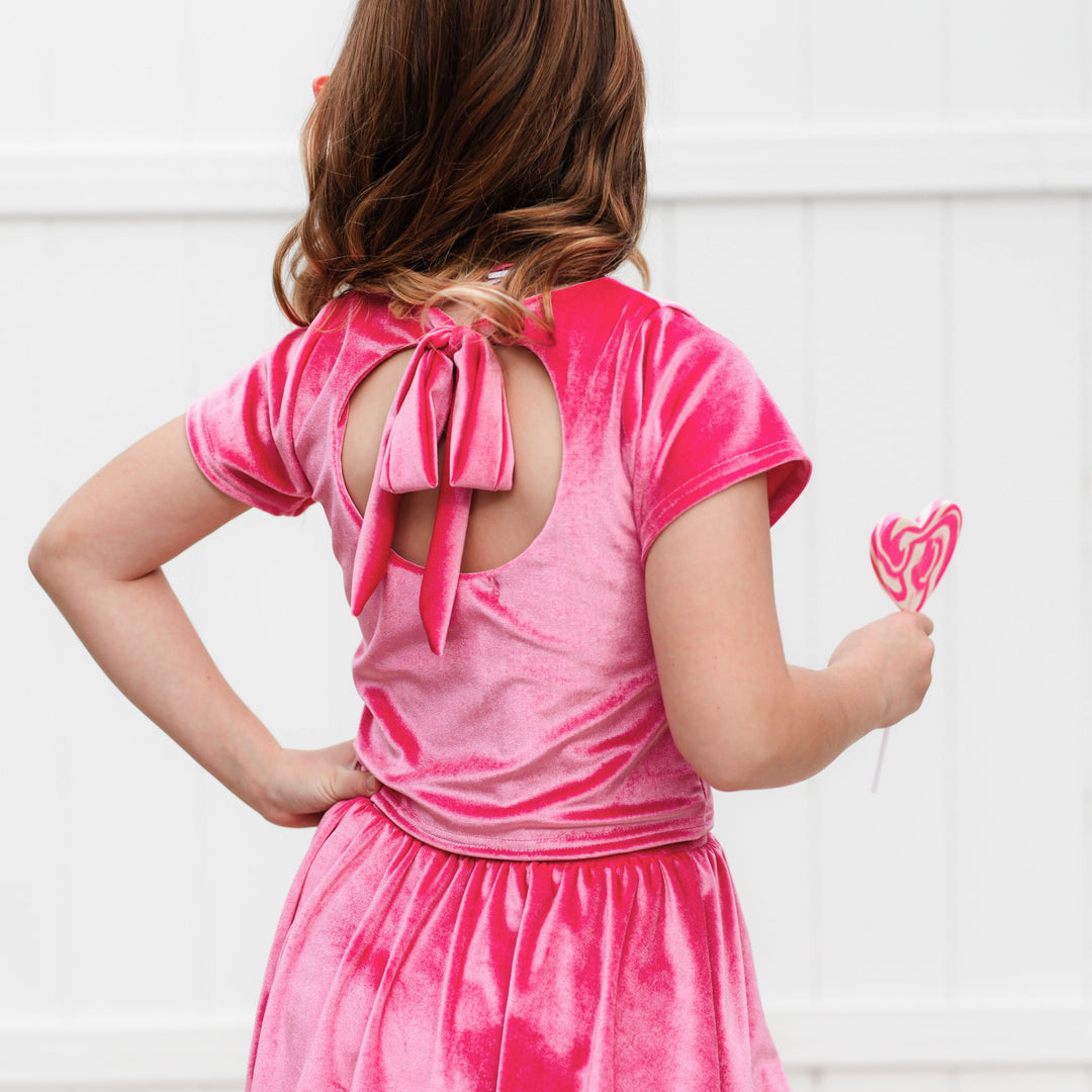 girl holding heart shaped sucker and facing away from camera to show keyhole cutout and bow tied back on pink velvet charm top