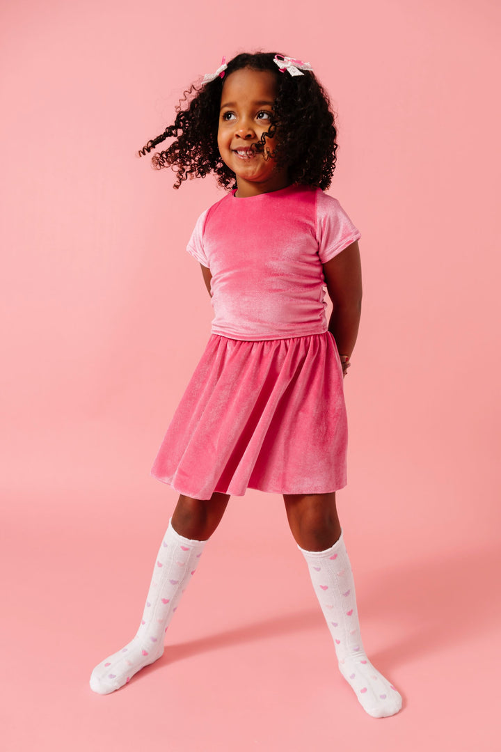 little girl in matching pink velvet fitted top and skort set with pastel heart knee high socks and matching white and pink lace ribbon pigtail bows