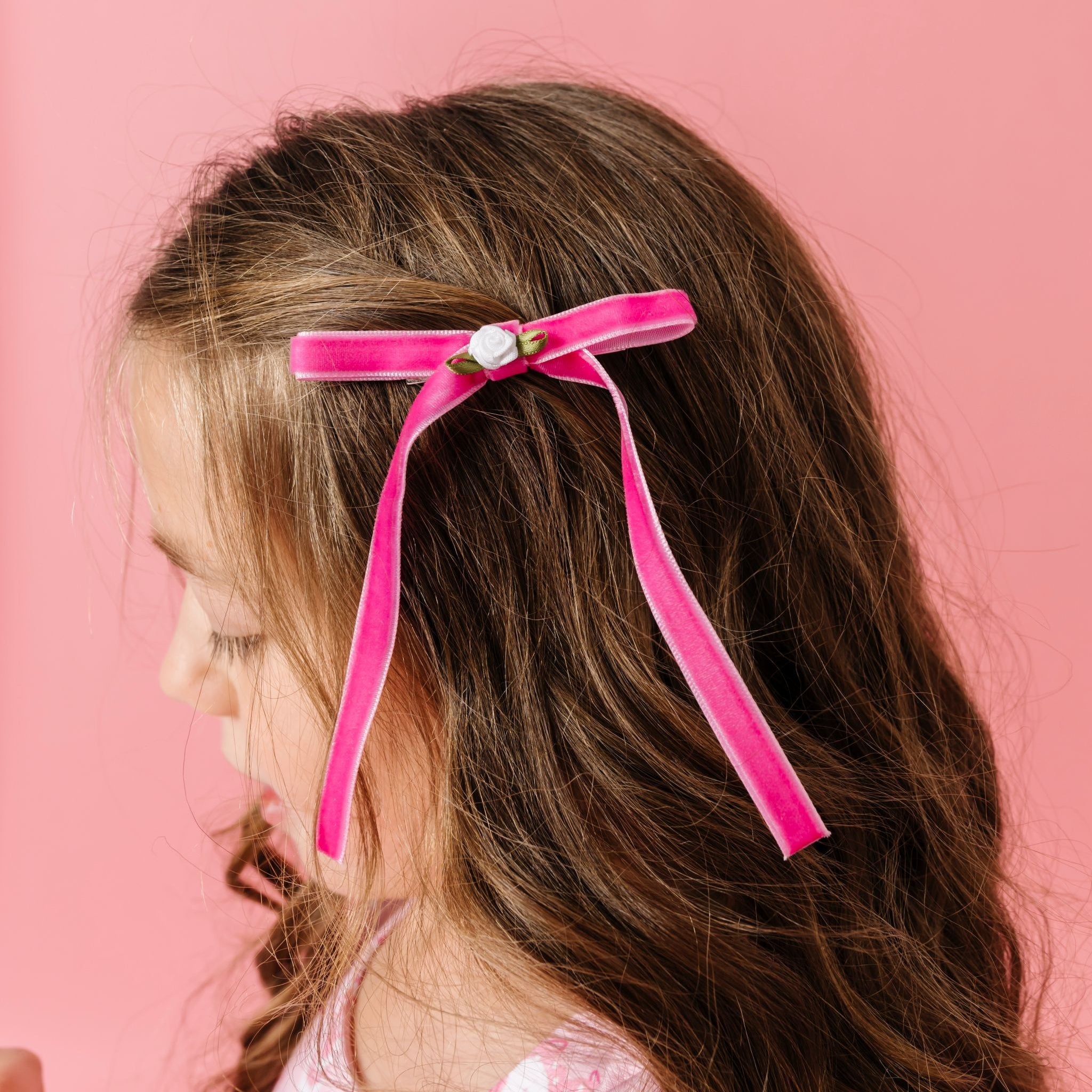 young girl wearing bright pink velvet ribbon hair bow with small white rosette at the center