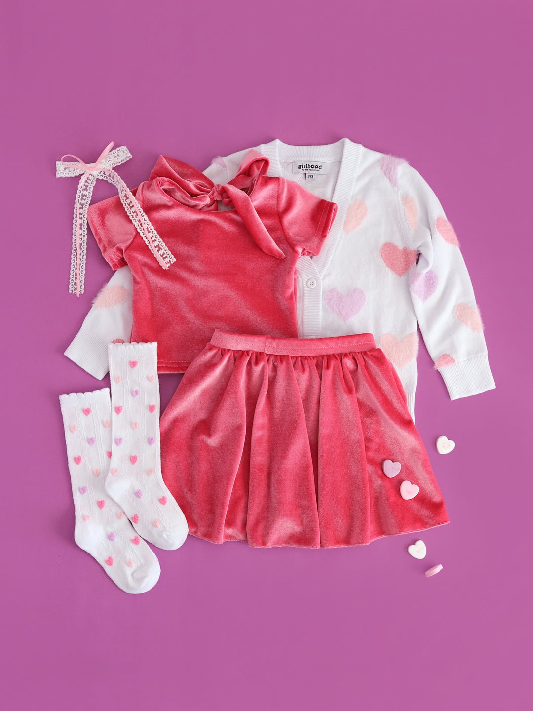 girls' pink velvet bow back top and skort set styled with white v-neck cardigan with fuzzy pastel hearts and matching white scalloped heart socks