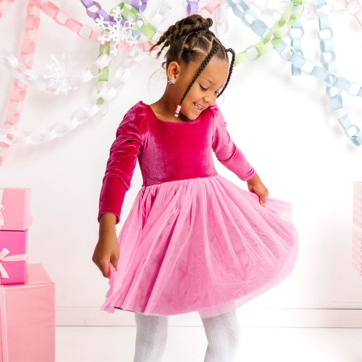 young girl in winter wonderland wearing pink velvet long sleeve dress with pink tutu skirt and white cable knit tights