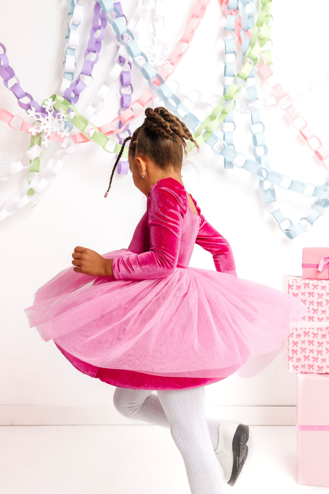 little girl twirling in pink velvet long sleeve party dress with pink tulle skirt and white cable knit tights
