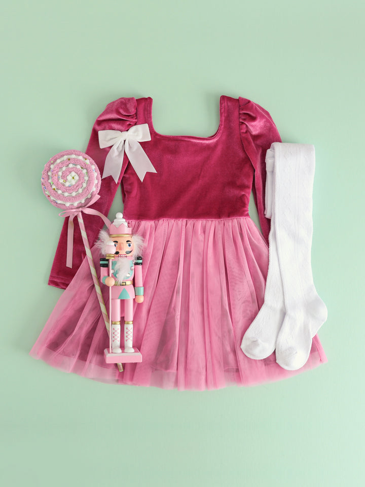 flat lay of pink long sleeve velvet dress with tulle skirt, white cable knit tights and white velvet ribbon bow beside nutcracker decoration