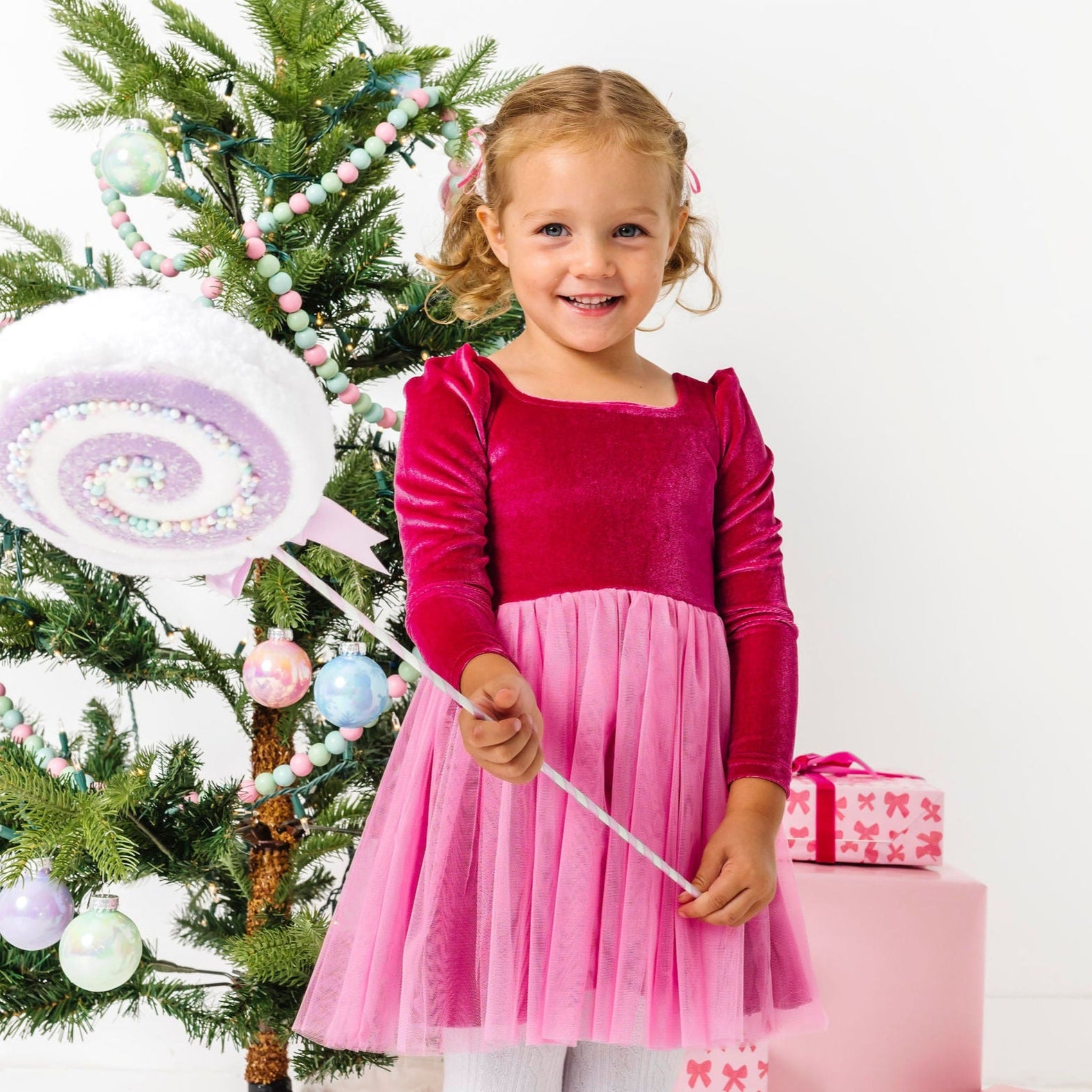 little girl holding lollipop in pink velvet party dress with pink tulle skirt styled for Christmas