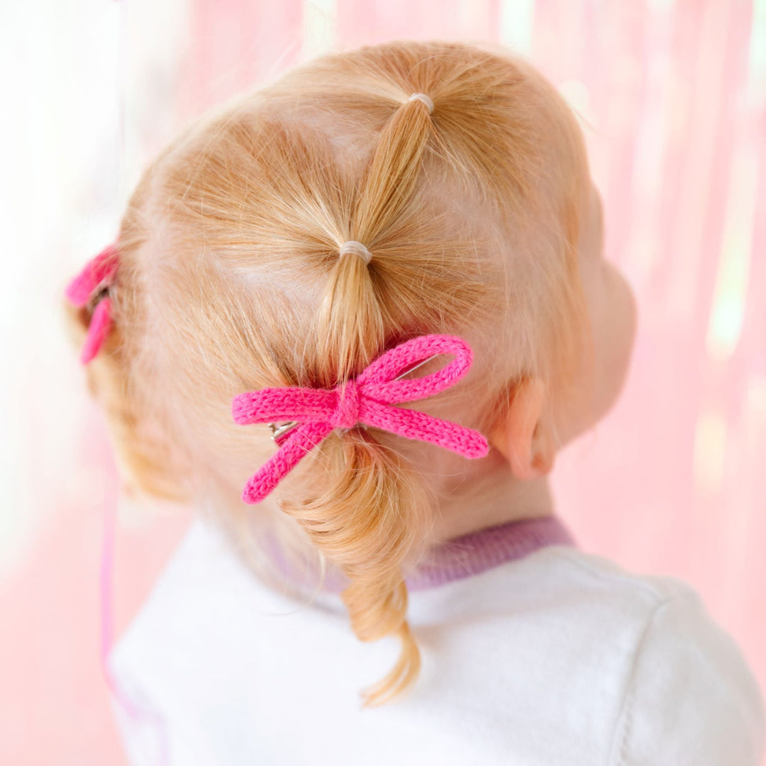 little girl in bright pink knit pigtail bows on clips and matching Valentine's sweater