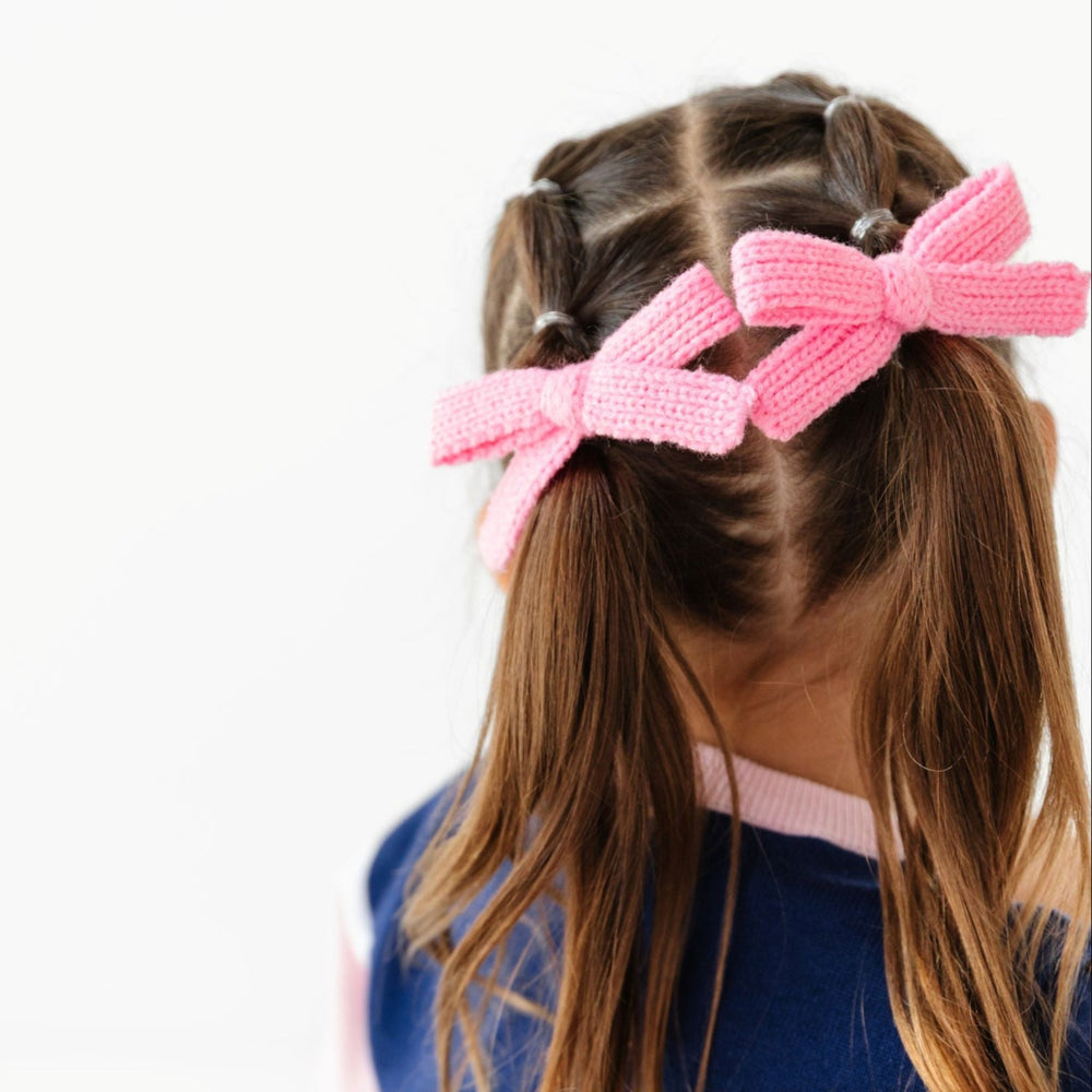 little girl in pigtails with set of two pink knit bows on clips