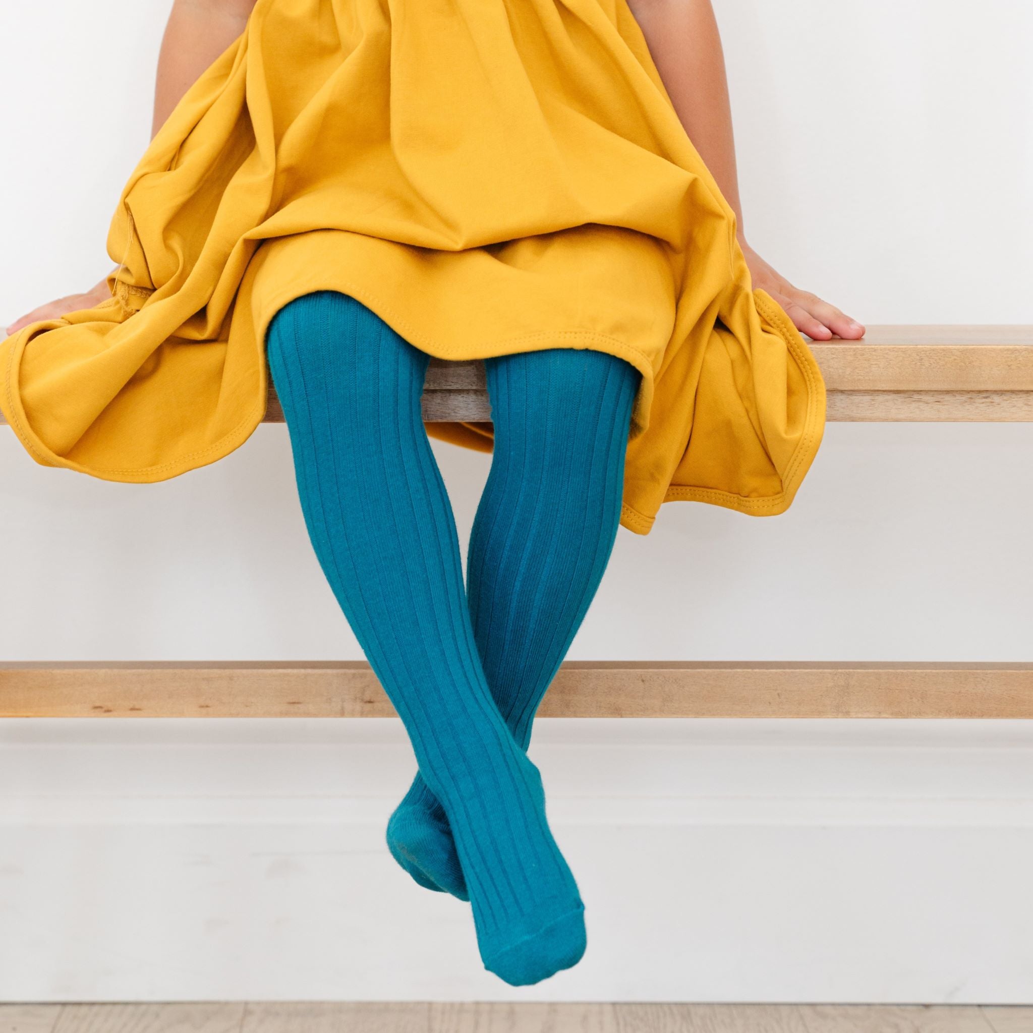 little girl with crossed legs wearing teal ribbed tights and mustard yellow dress