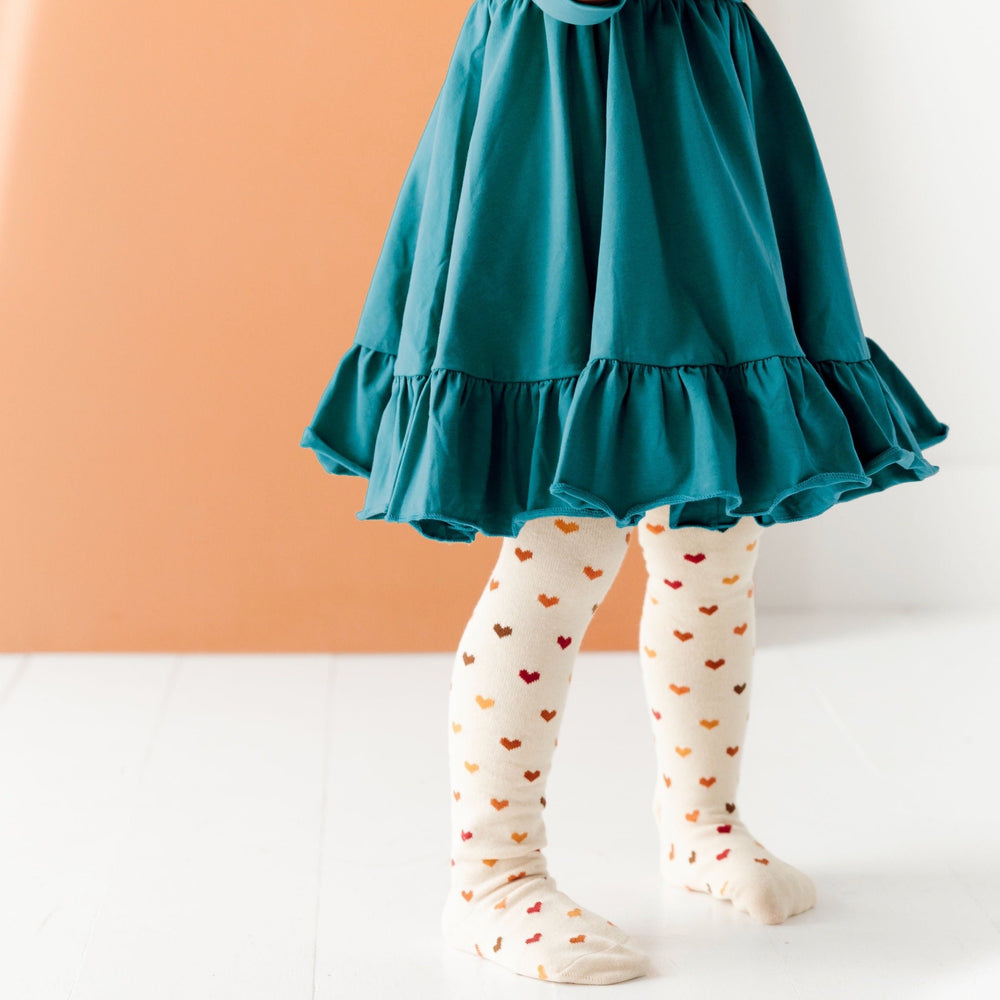 little girl wearing teal long sleeve dress with fall colored heart pattern tights