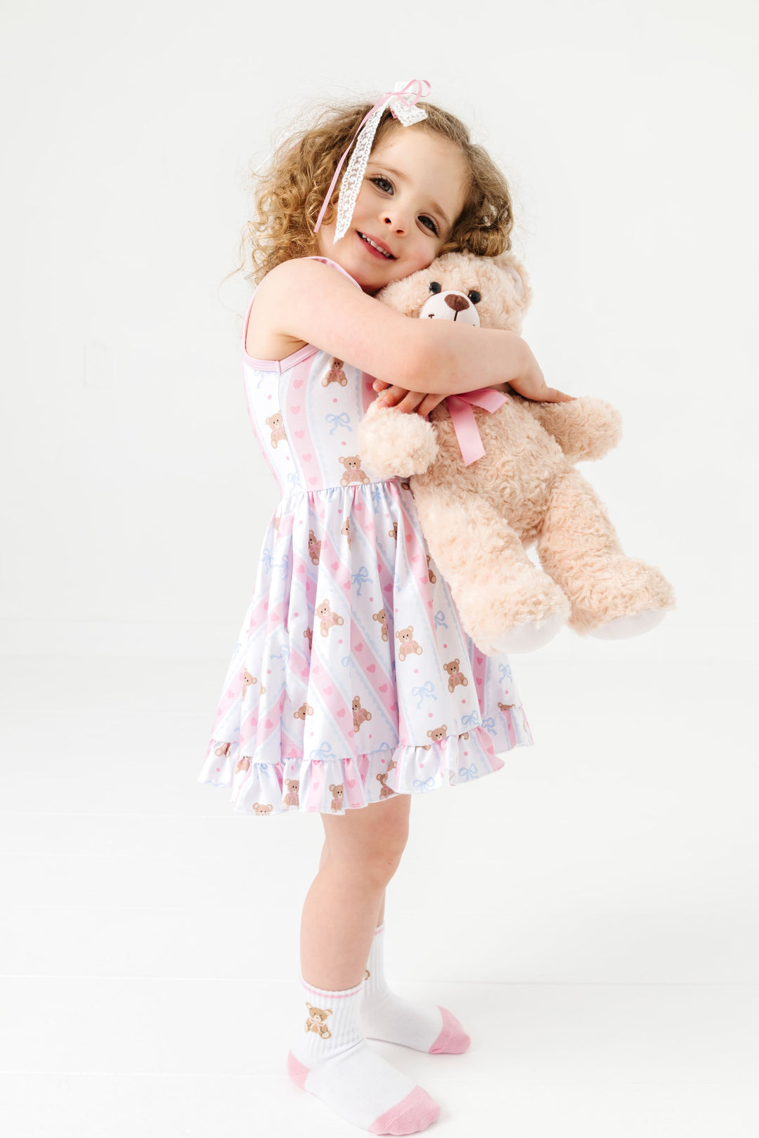 little girl hugging teddy bear in teddy print summer twirl dress and matching teddy bear crew socks