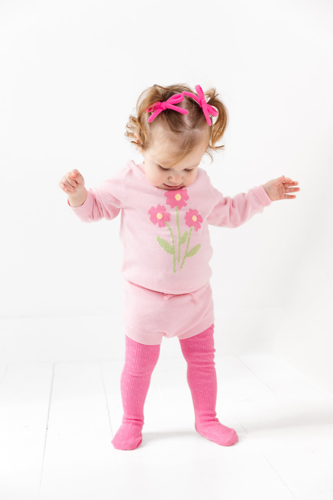 toddler girl in spring outfit of blossom pink flower sweater and matching knit bloomers and taffy pink cable knit tights