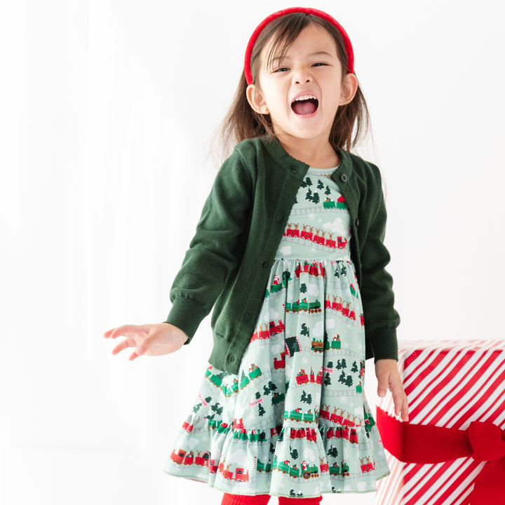 girl wearing christmas train print dress with matching forest green cardigan