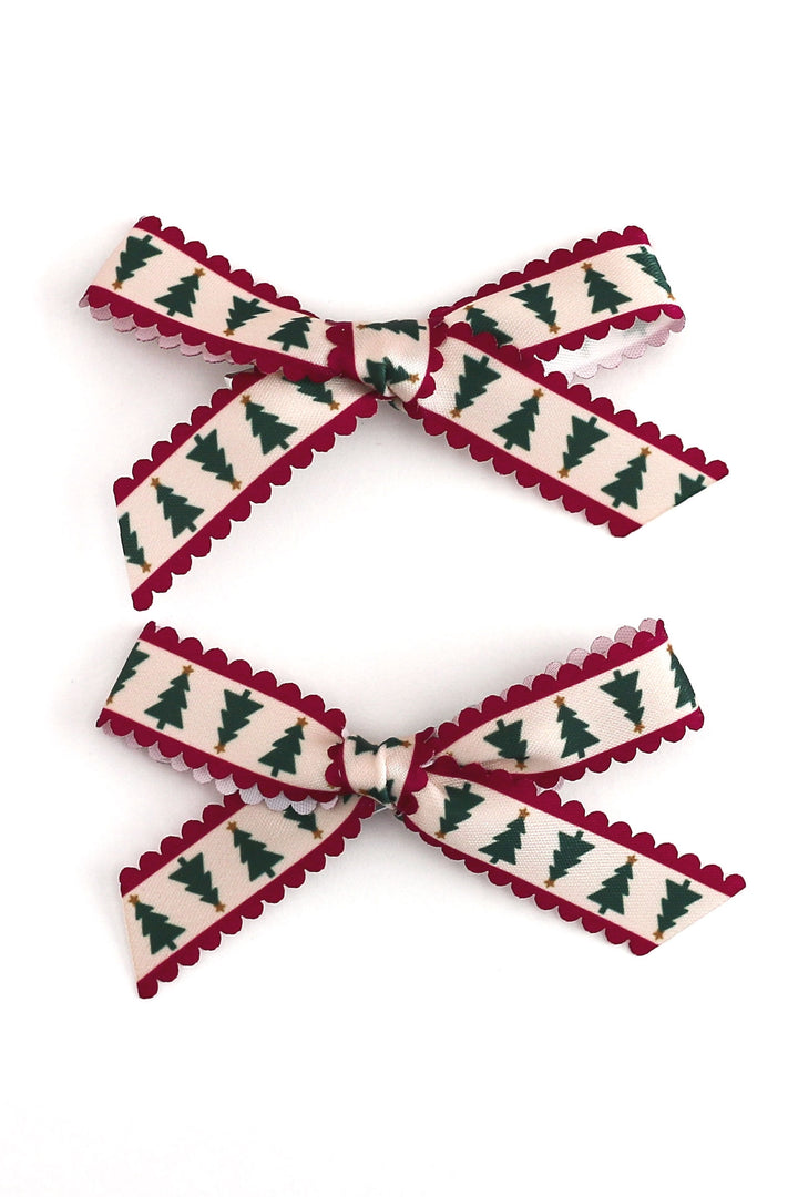 Two matching ribbon hair bows with a Christmas tree pattern, featuring a cream background, dark green pine trees, and a deep red scalloped edge, displayed on a clean white background.
