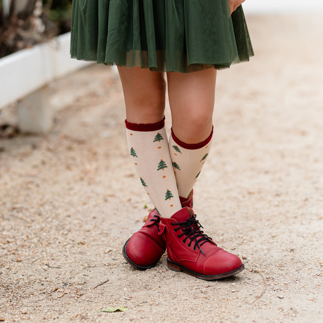 girl in red boots and forest green tutu skirt paired with cream knee highs with crimson scalloped trim and Christmas tree pattern