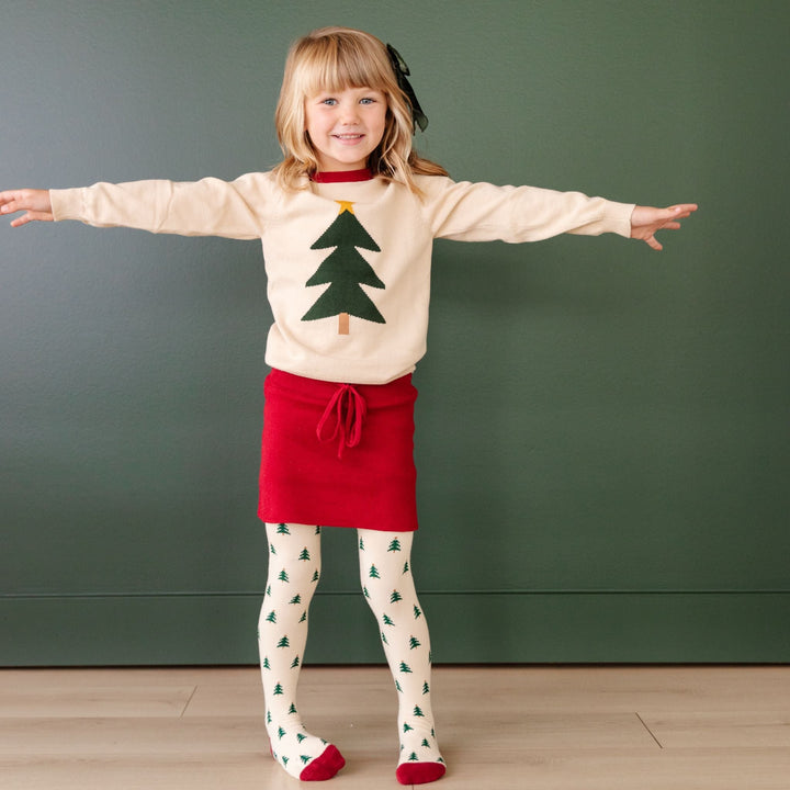 little girl in matching Christmas tree knit set with pullover sweater, sweater skirt and tights