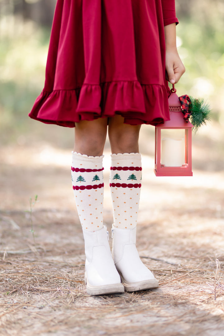 little girl in Christmas tree themed knee highs socks and matching red cotton dress