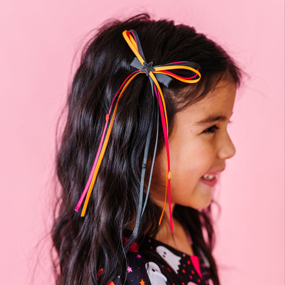little girl in ghost print twirl dress wearing matching orange, pink and black ribbon bow with tiny star embellishments on clip