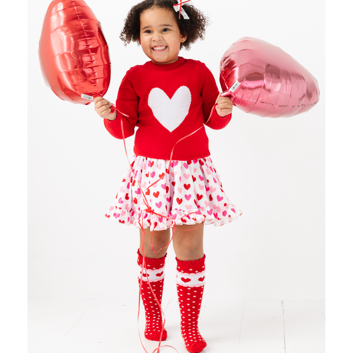 girl holding balloons white dress with red and pink heart print and red sweater with white heart and valentine's day patterned knee highs