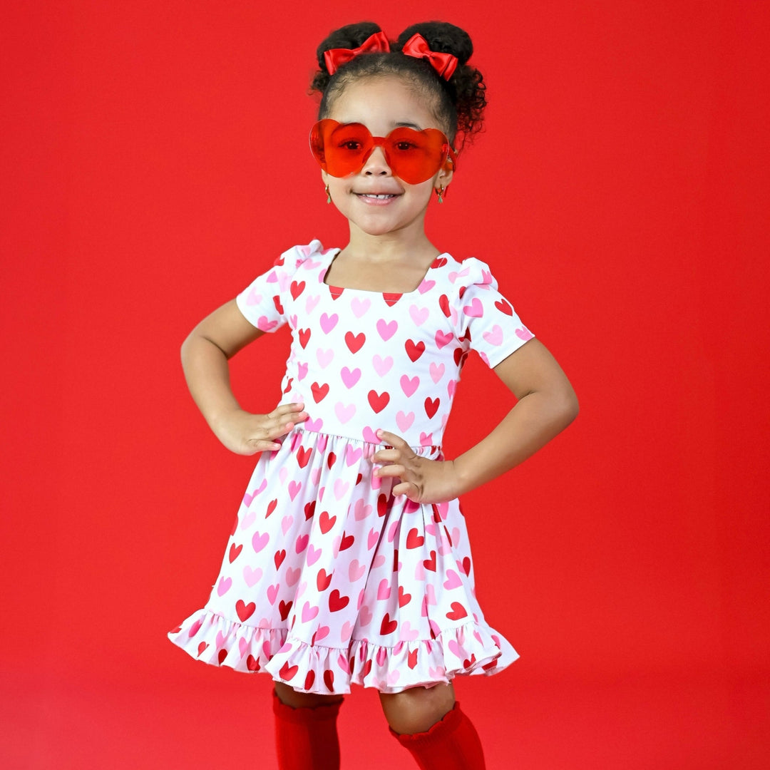 girl in square neck twirl dress that is white with pink and red heart pattern