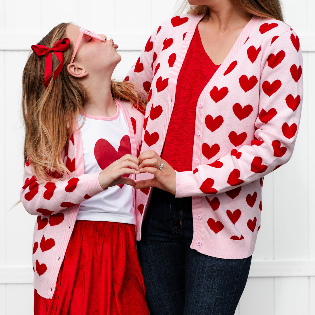 young girl and mother in matching mommy and me light pink cotton knit cardigans with red heart pattern for Valentine's Day