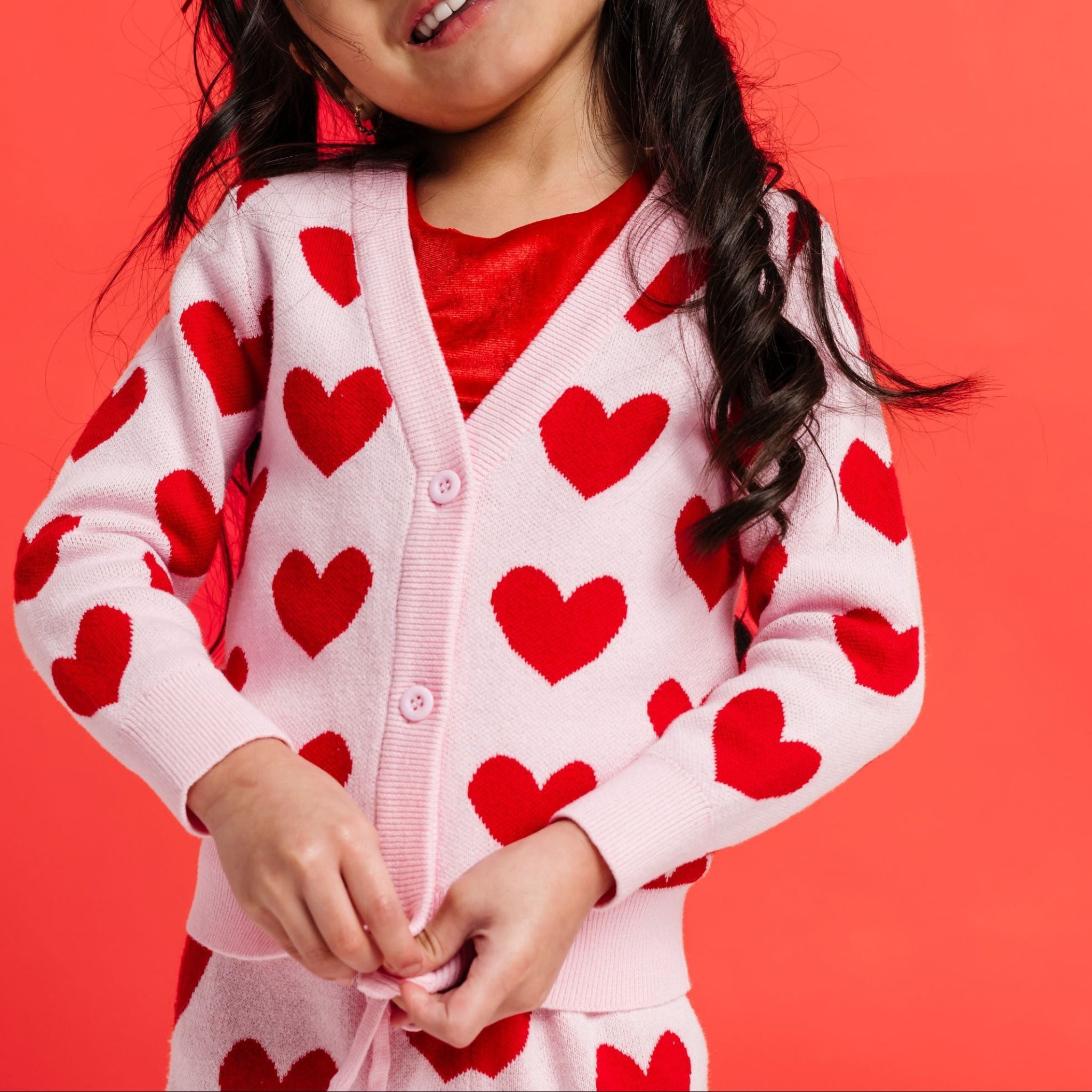 young girl with blossom pink knit cardigan buttoned over bright red velvet top paired with matching sweater pants