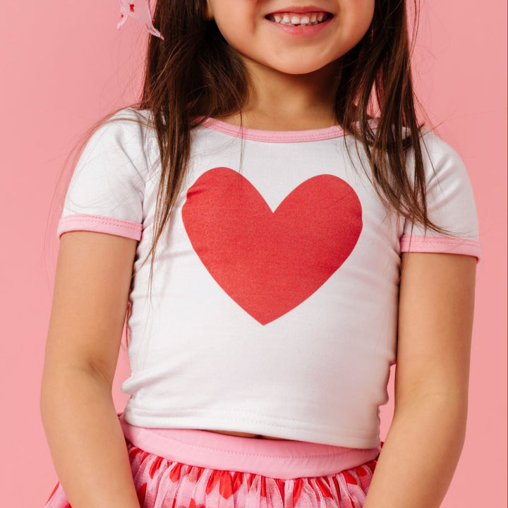 little girl in white bamboo fitted top with red heart design and light pink trim paired with heart tutu skirt for Valentine's Day