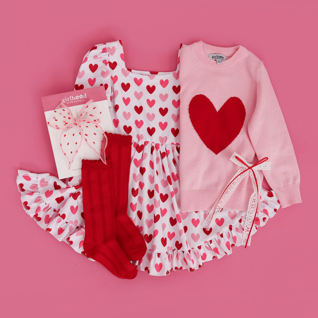 flat lay of girls Valentine's twirl dress with pink and red hearts, pink with red heart sweater and matching socks and bows