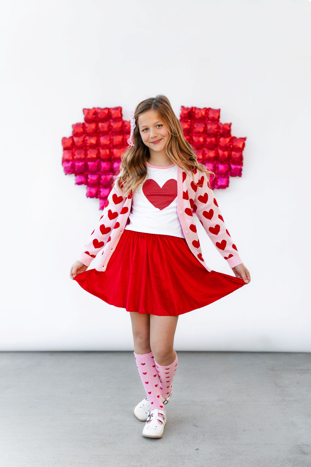 girl wearing pinkand red heart cardigan and matching knee highs paired with red heart bamboo top and red velvet skort for valentines day